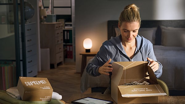 woman opening a package in a living room with other packages on the table next to her